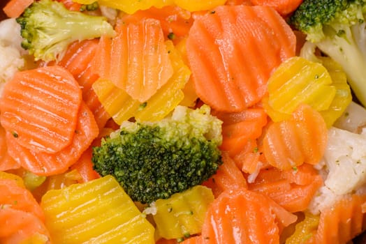 Delicious fresh vegetables steamed carrots, broccoli, cauliflower on a black plate on a dark concrete background
