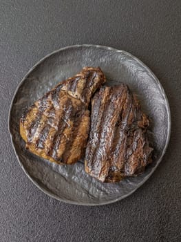 Grilled beef steak with salt, spices and herbs on dark concrete background