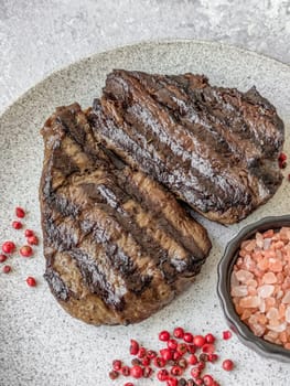 Grilled beef steak with salt, spices and herbs on dark concrete background