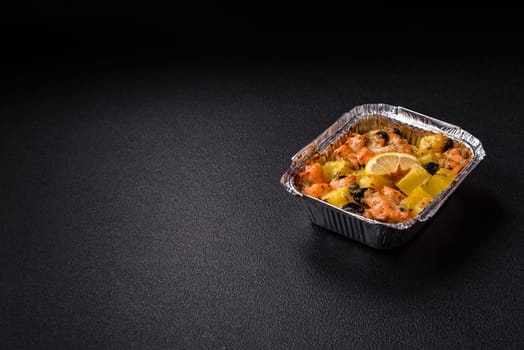 Baked salmon pieces with potatoes, cheese and olives with salt, spices and herbs on a dark concrete background