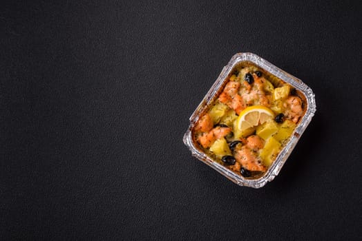 Baked salmon pieces with potatoes, cheese and olives with salt, spices and herbs on a dark concrete background