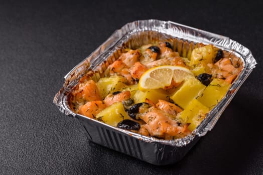 Baked salmon pieces with potatoes, cheese and olives with salt, spices and herbs on a dark concrete background