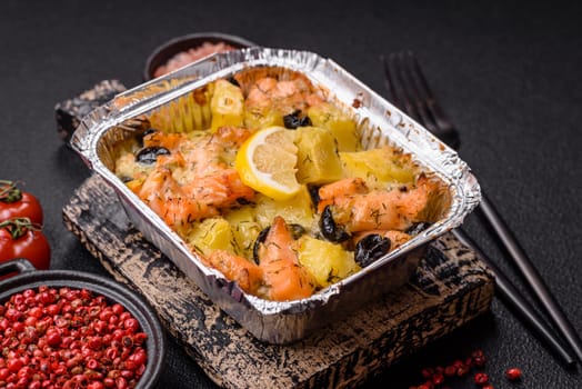 Baked salmon pieces with potatoes, cheese and olives with salt, spices and herbs on a dark concrete background
