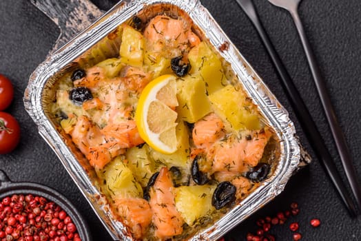 Baked salmon pieces with potatoes, cheese and olives with salt, spices and herbs on a dark concrete background
