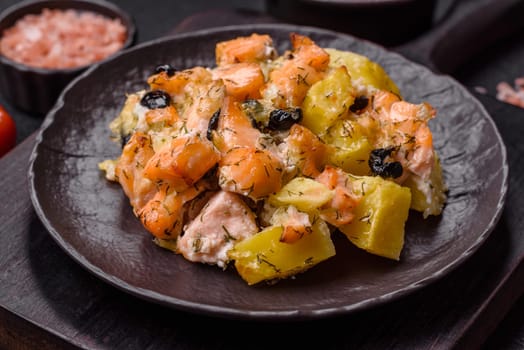 Baked salmon pieces with potatoes, cheese and olives with salt, spices and herbs on a dark concrete background