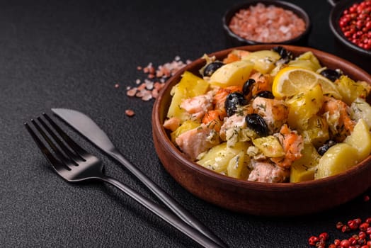 Baked salmon pieces with potatoes, cheese and olives with salt, spices and herbs on a dark concrete background