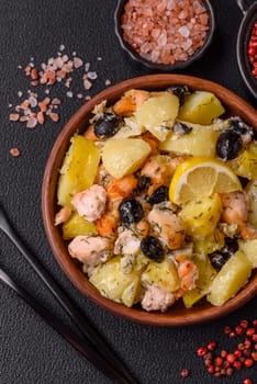 Baked salmon pieces with potatoes, cheese and olives with salt, spices and herbs on a dark concrete background