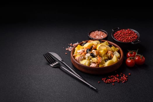 Baked salmon pieces with potatoes, cheese and olives with salt, spices and herbs on a dark concrete background