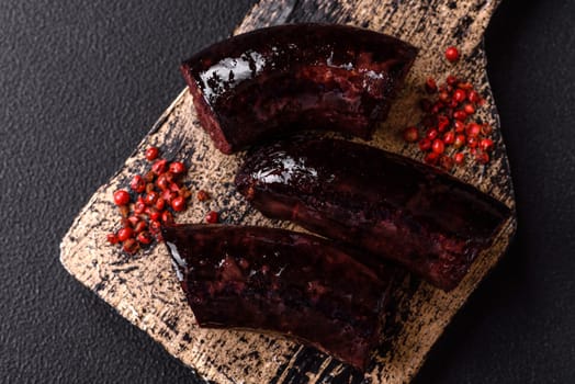 Delicious black blood sausage or black pudding with spices and herbs grilled on a black concrete background