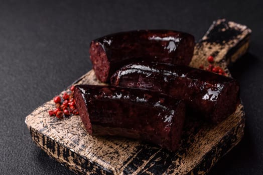 Delicious black blood sausage or black pudding with spices and herbs grilled on a black concrete background