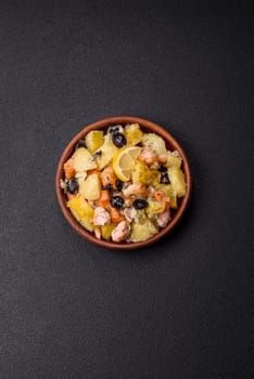 Baked salmon pieces with potatoes, cheese and olives with salt, spices and herbs on a dark concrete background
