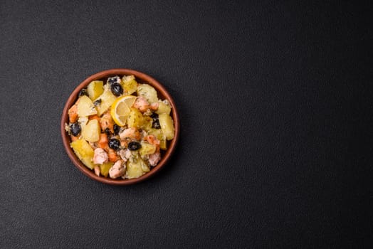 Baked salmon pieces with potatoes, cheese and olives with salt, spices and herbs on a dark concrete background