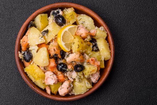 Baked salmon pieces with potatoes, cheese and olives with salt, spices and herbs on a dark concrete background
