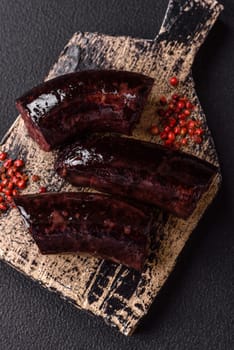 Delicious black blood sausage or black pudding with spices and herbs grilled on a black concrete background