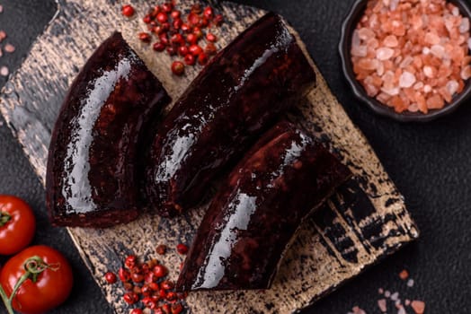 Delicious black blood sausage or black pudding with spices and herbs grilled on a black concrete background