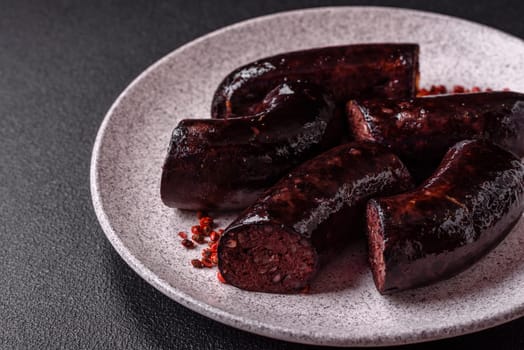 Delicious black blood sausage or black pudding with spices and herbs grilled on a black concrete background