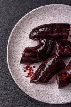 Delicious black blood sausage or black pudding with spices and herbs grilled on a black concrete background