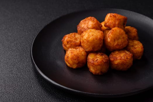 Delicious fried potato balls or croquettes with salt, spices and herbs on a dark concrete background