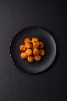 Delicious fried potato balls or croquettes with salt, spices and herbs on a dark concrete background