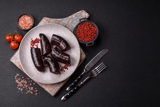 Delicious black blood sausage or black pudding with spices and herbs grilled on a black concrete background