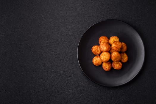 Delicious fried potato balls or croquettes with salt, spices and herbs on a dark concrete background