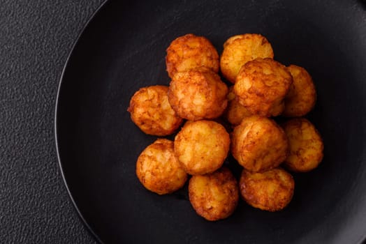 Delicious fried potato balls or croquettes with salt, spices and herbs on a dark concrete background