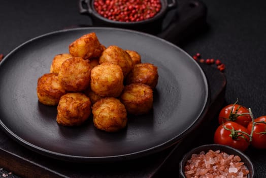 Delicious fried potato balls or croquettes with salt, spices and herbs on a dark concrete background