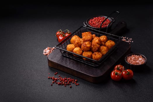 Delicious fried potato balls or croquettes with salt, spices and herbs on a dark concrete background