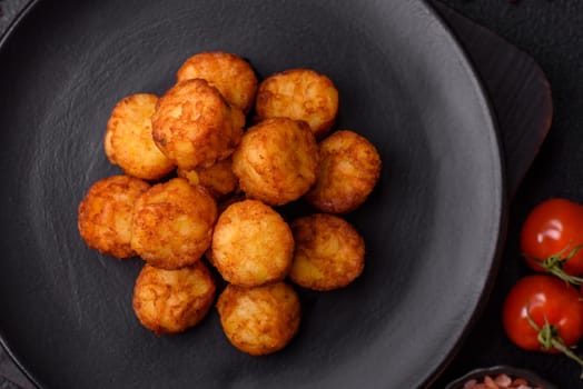 Delicious fried potato balls or croquettes with salt, spices and herbs on a dark concrete background