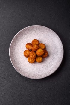 Delicious fried potato balls or croquettes with salt, spices and herbs on a dark concrete background