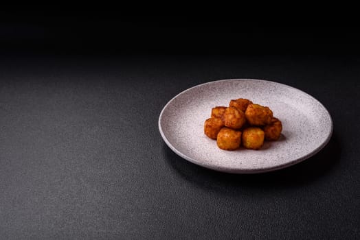 Delicious fried potato balls or croquettes with salt, spices and herbs on a dark concrete background