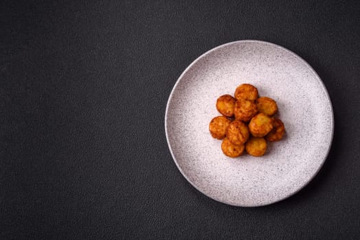 Delicious fried potato balls or croquettes with salt, spices and herbs on a dark concrete background