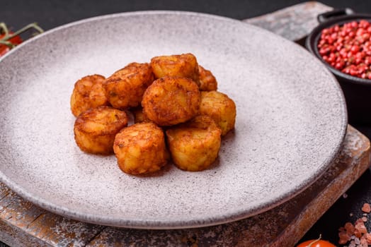 Delicious fried potato balls or croquettes with salt, spices and herbs on a dark concrete background