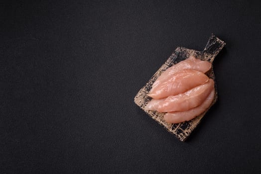Raw chicken fillet cut into strips with spices and herbs on a wooden cutting board