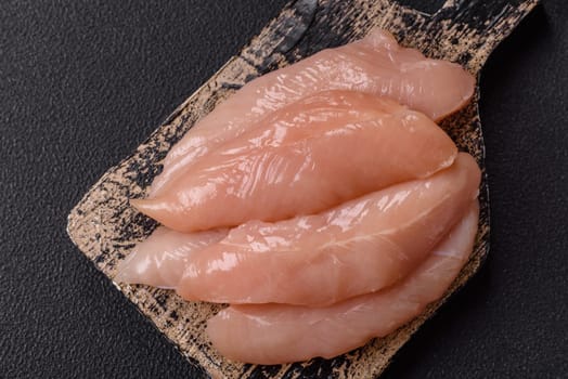 Raw chicken fillet cut into strips with spices and herbs on a wooden cutting board