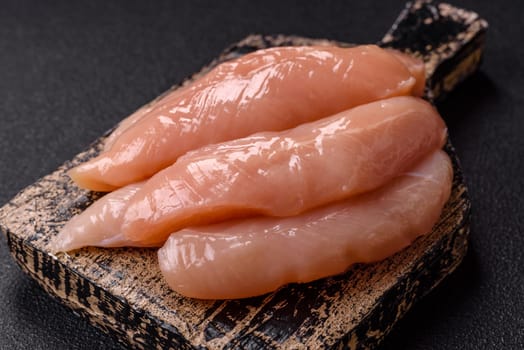 Raw chicken fillet cut into strips with spices and herbs on a wooden cutting board