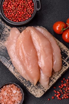 Raw chicken fillet cut into strips with spices and herbs on a wooden cutting board