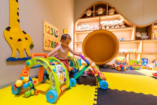 Child playing in a vibrant indoor playroom with activity walkers, developmental toys, and interactive learning equipment for fun and growth