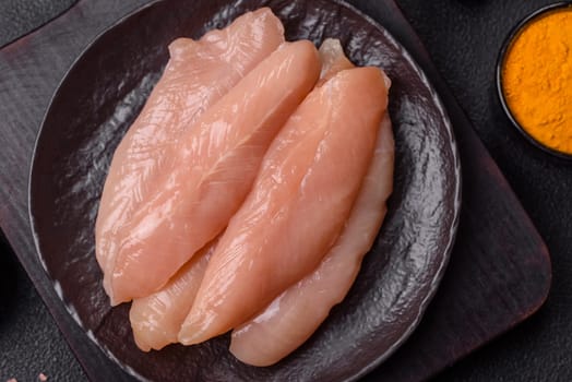 Raw chicken fillet cut into strips with spices and herbs on a wooden cutting board