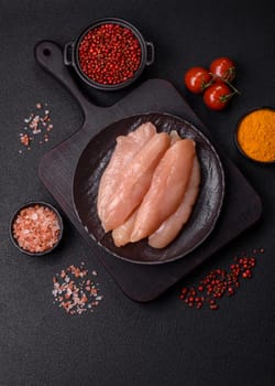 Raw chicken fillet cut into strips with spices and herbs on a wooden cutting board