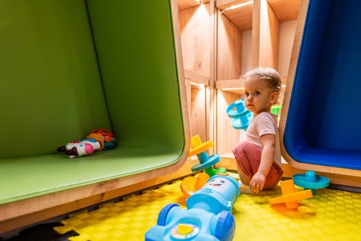 Curious toddler playing in modern playroom with colorful shelves, activity toys, and cozy seating for creative learning