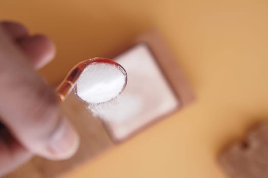 A detailed closeup of a hand holding a spoonful of sugar above an empty container