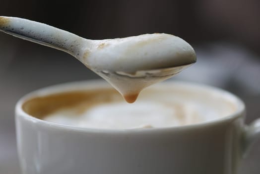 This is a detailed closeup image of a spoon skillfully lifting frothy milk from a coffee cup