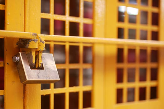 A vibrant yellow gate, secured with a sturdy padlock, features a distinctive gridded pattern