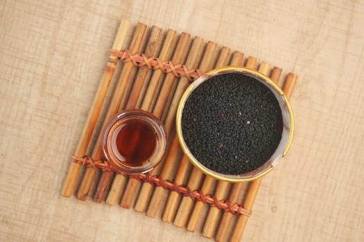 An oil bottle is in the background, and black seeds are showcased in a wooden bowl