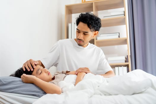 Side view Asian young father sit near his son lie on bed with sick or unwell and father take care with love and support.