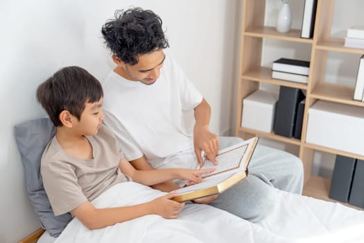 Top view Asian young father sit near his son on bed and read the book together with happiness and day light.