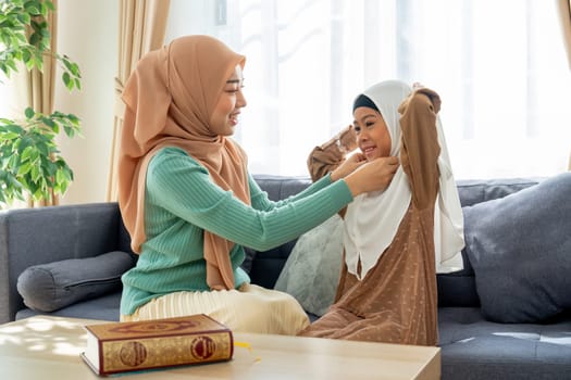 Side view of muslim mother help her daughter to wear headscarf or hijab for her and stay in living room of their house with day light and happiness.