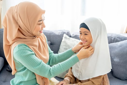 Close up Asian muslim mother help her daughter to wear headscarf or hijab for her and stay in living room of their house with day light and happiness.