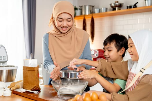 Side view little boy and girl of muslim family help and learn from their mother to cook relate to cooking flour and ingredients in the kitchen with happiness.
